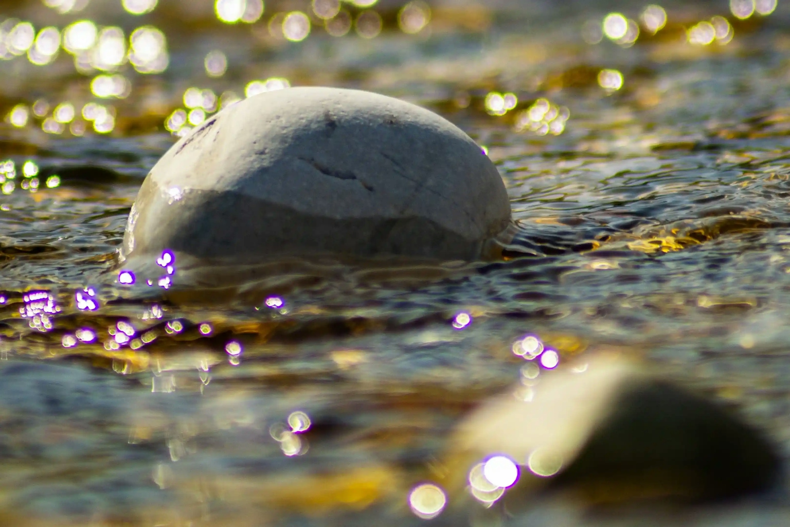 Roccia bianca parzialmente sommersa in fiume luccicante d'oro e violetto